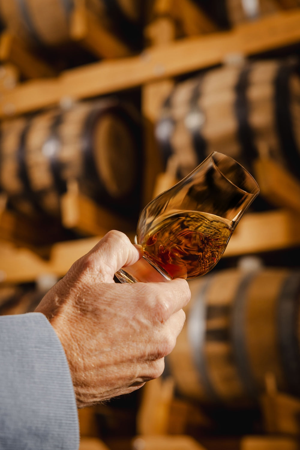Single Malt Whisky in a tasting glass being swirled around with Hillwood Whisky casks in the background.